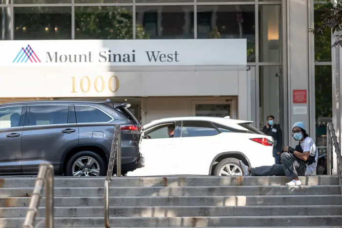 A man wearing a mask sits on the steps outside Mount Sinai West Hospital.
